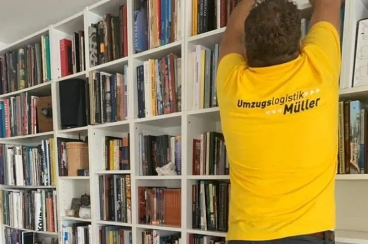 umzugshelfer ordnet buecherregal im wohnraum
